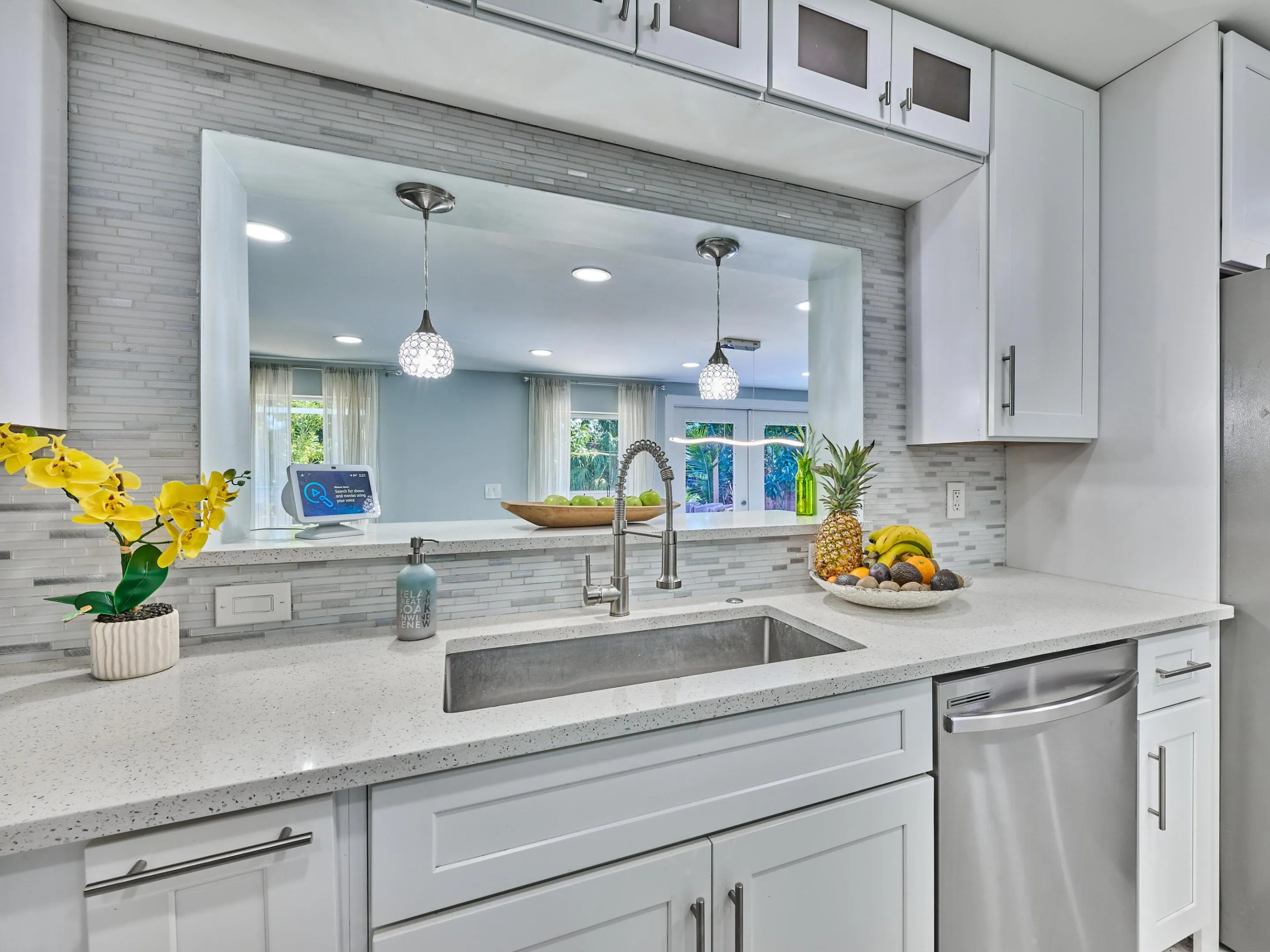 White shaker-style cabinetry with dark pulls, stone-finish countertops, stainless steel sink with gooseneck faucet, full-size stainless steel dishwasher, and a light-toned tile backsplash