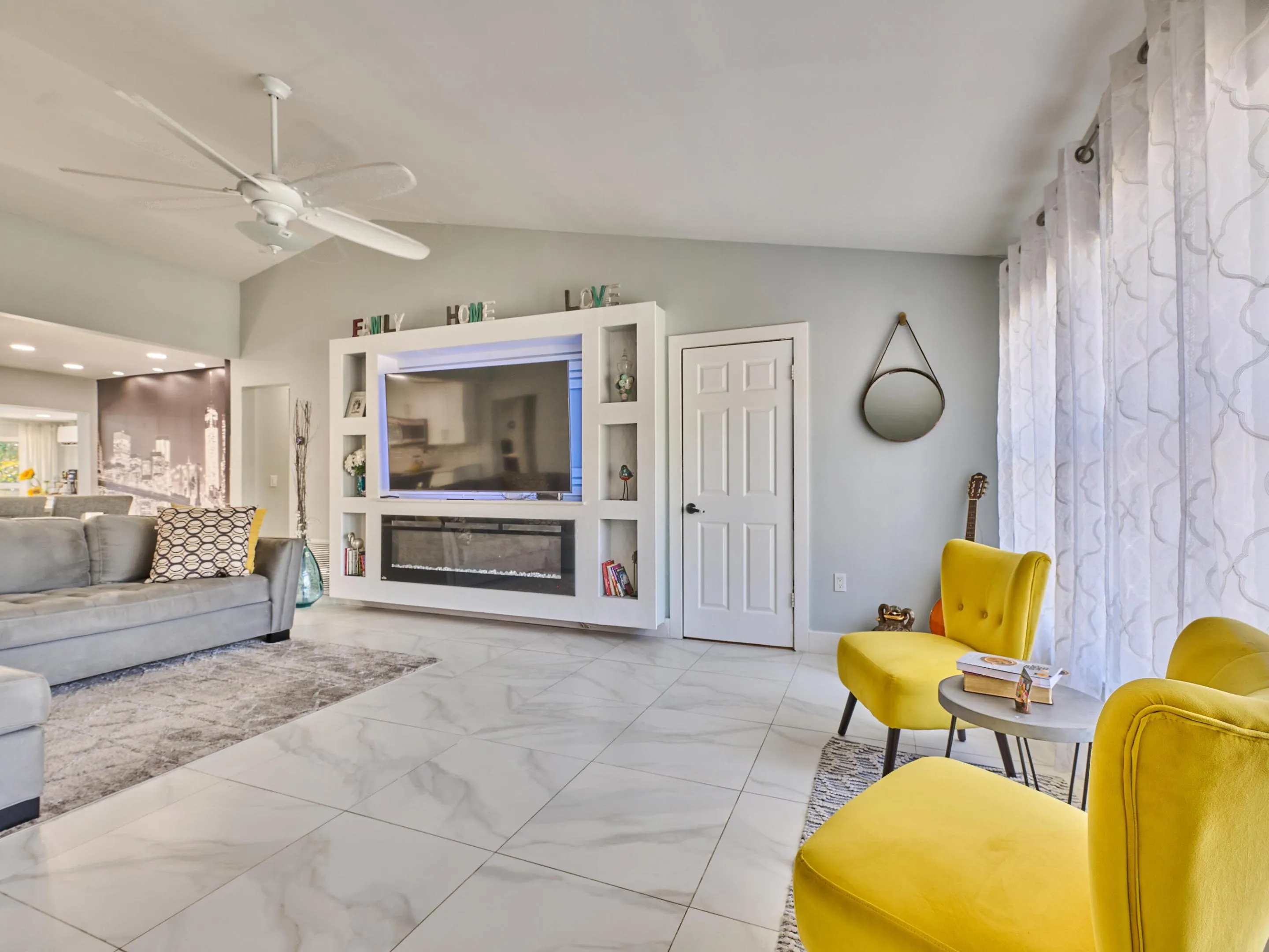 Spacious living area featuring large format tile flooring, a built-in media console with integrated fireplace, and a ceiling fan