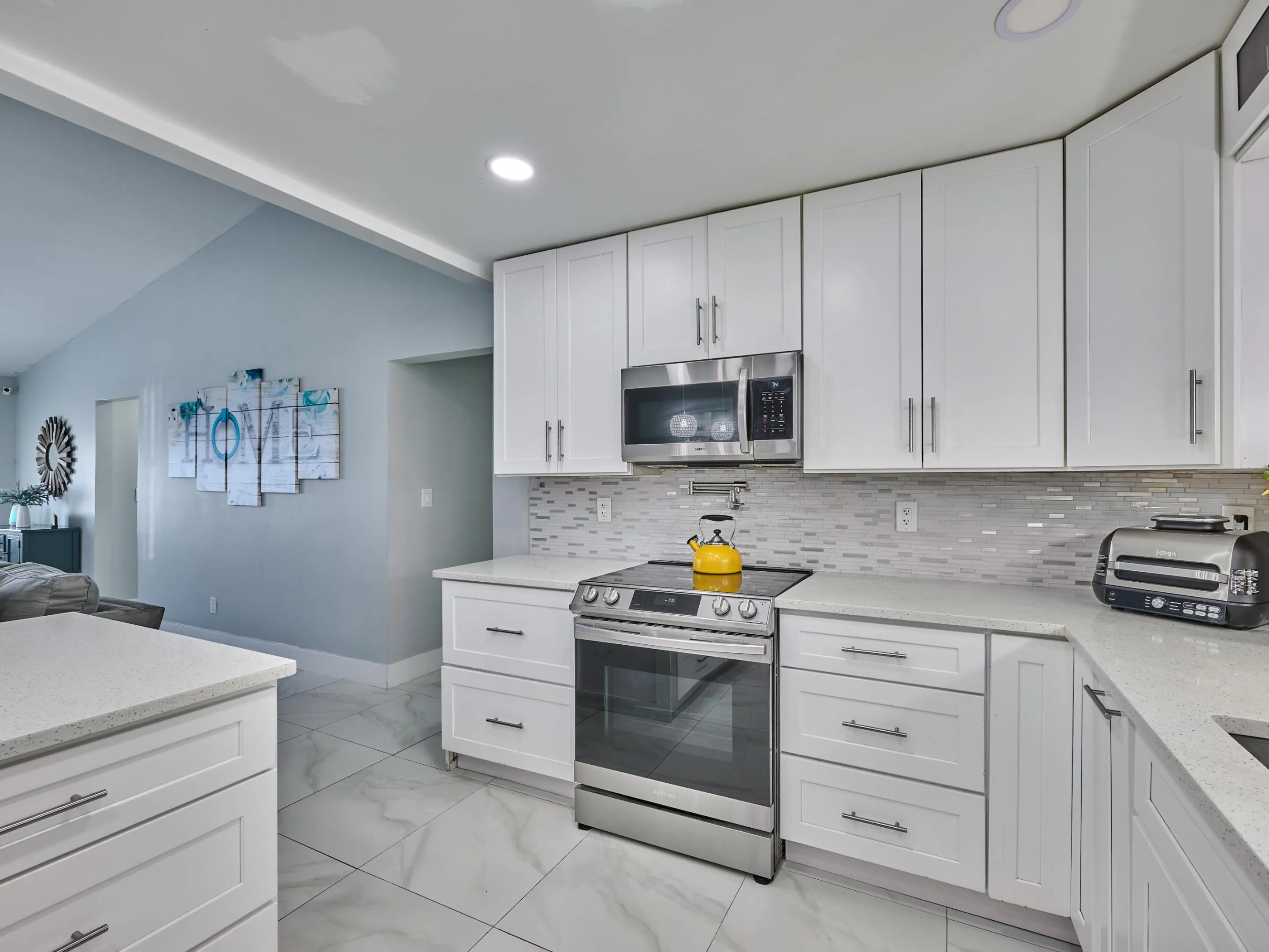 White shaker cabinetry, stainless steel appliances, quartz countertops, tile backsplash, and large format tile flooring