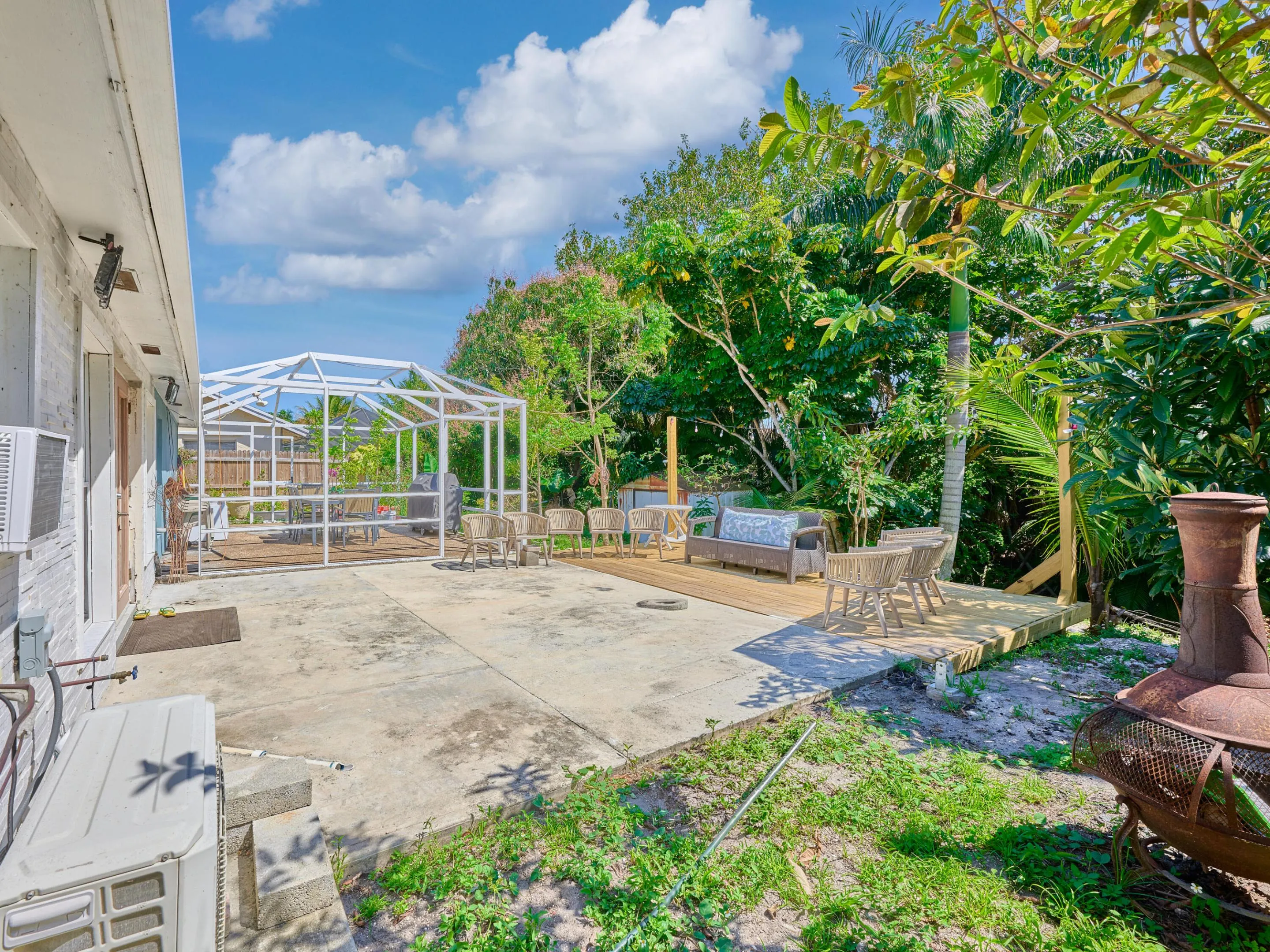 Concrete patio with an adjacent wood deck, a screened enclosure, and mature landscaping