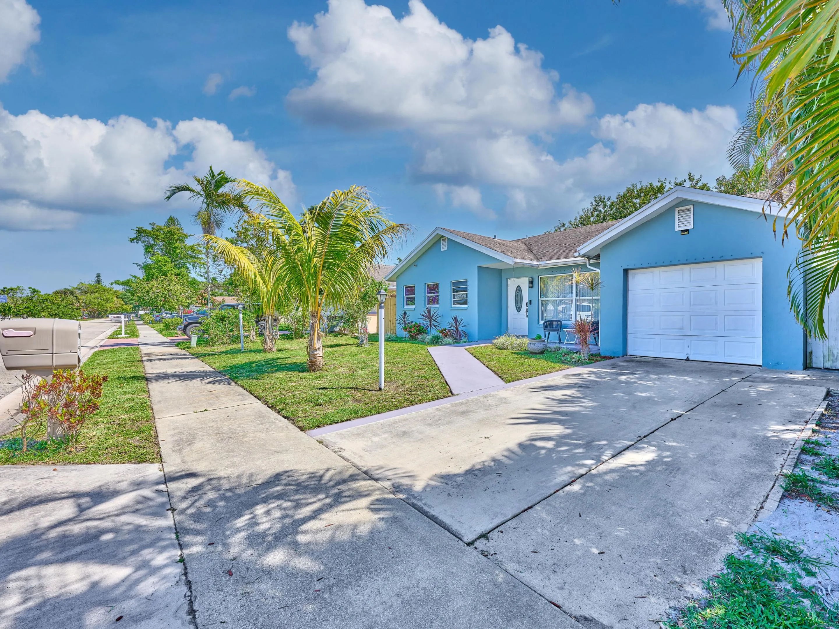 Single-story residence featuring a blue exterior, a covered entryway, a white garage door, and a concrete driveway