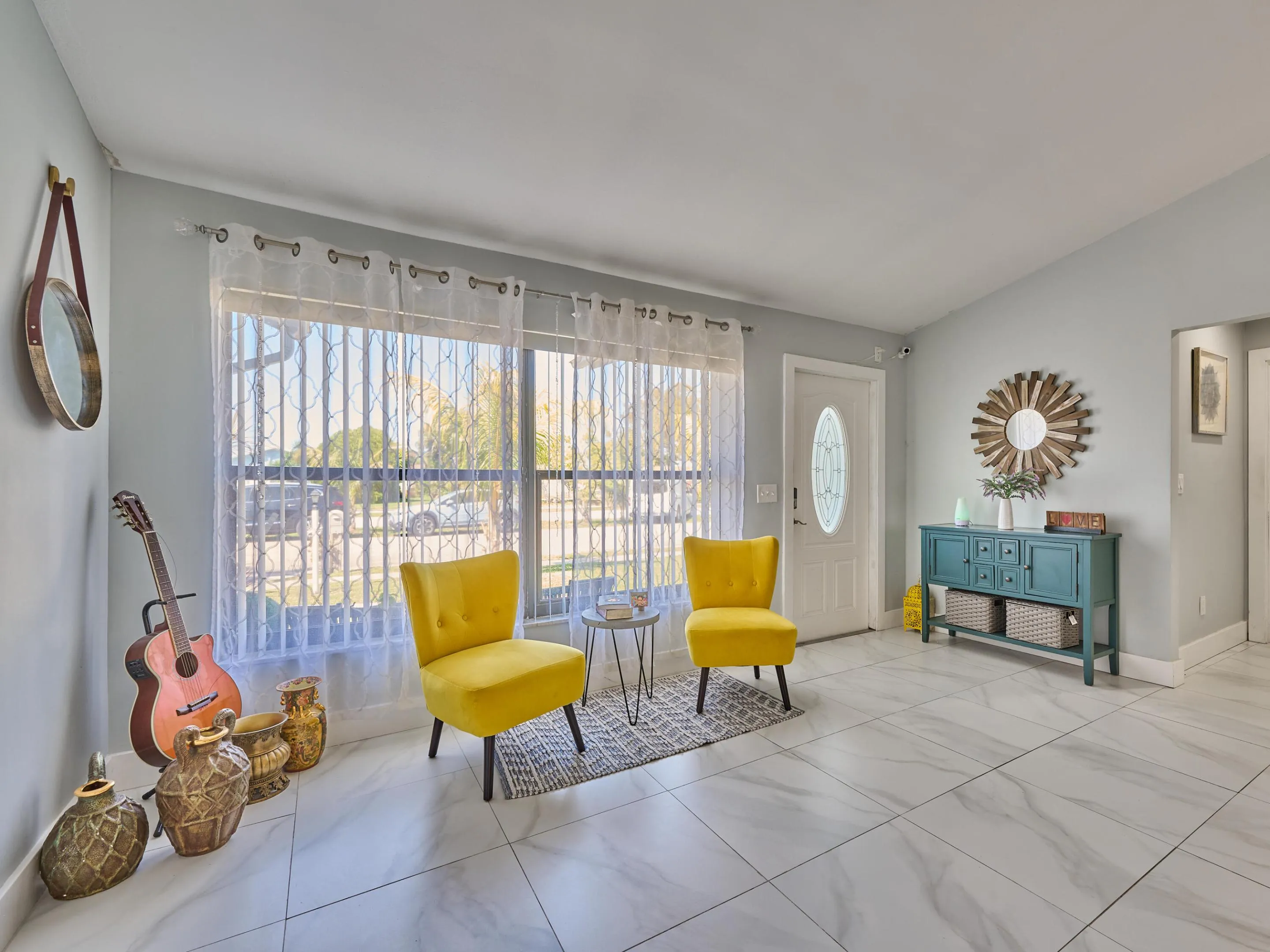 White tile flooring with subtle veining, large front window with vertical blinds, oval-insert entry door, and vaulted ceiling
