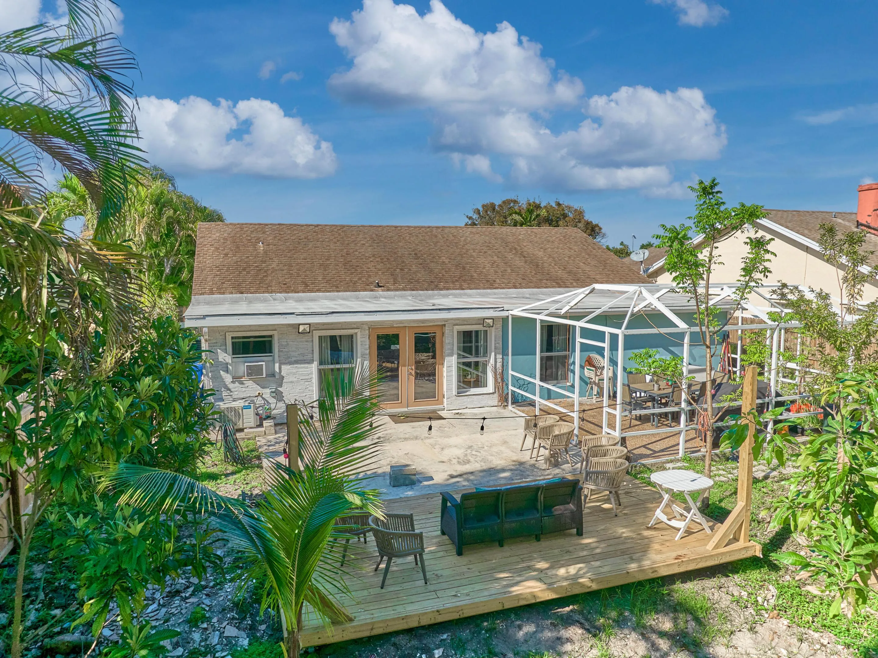 Spacious backyard with a wooden deck, covered patio, and mature tropical landscaping