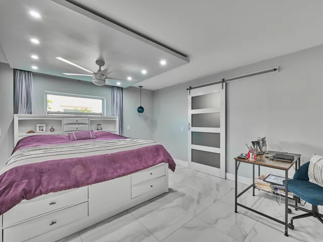 Recessed lighting, ceiling fan, white barn door with frosted glass panels, built-in storage headboard, and white tile flooring