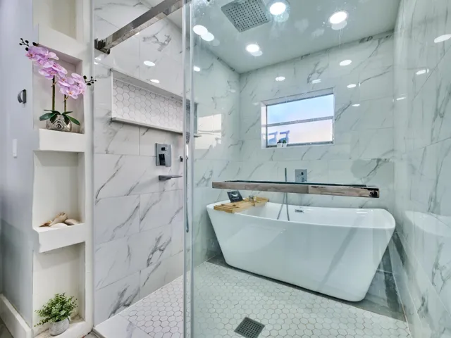 Freestanding soaking tub, floor-to-ceiling marble-look tile, glass-enclosed shower, rain shower head, and recessed wall shelving