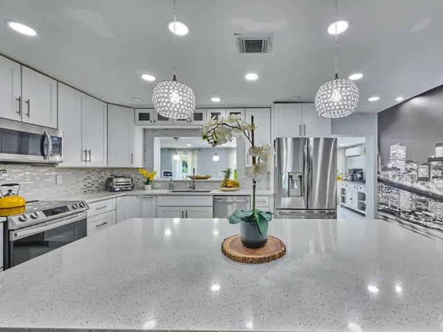 Contemporary kitchen featuring white cabinetry with chrome hardware, stainless steel appliances including a French-door refrigerator and gas cooktop, quartz countertops with waterfall edge detail, subway tile backsplash, dual pendant lighting with textured glass shades, recessed ceiling lights, and a large center island with seating