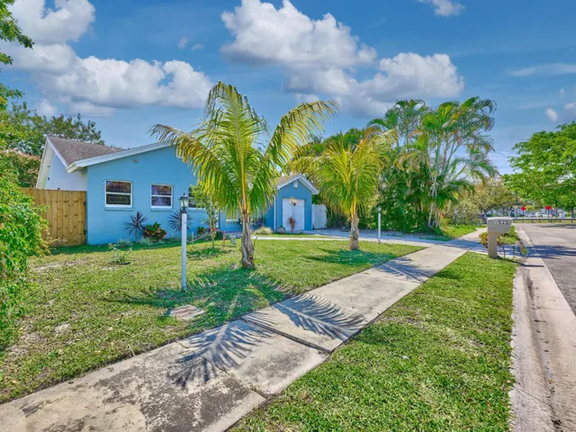 Blue exterior, white-framed windows, wood fencing, mature palm trees, and sidewalk access
