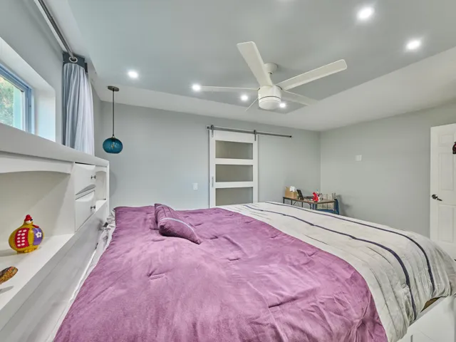 Recessed ceiling lighting, ceiling fan, built-in shelving, opaque panel sliding door, and white paneled door with black hardware