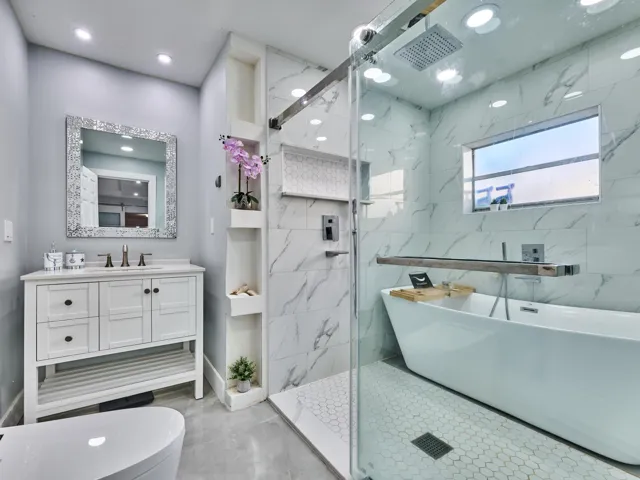 Freestanding soaking tub, walk-in shower with glass enclosure, white vanity with integrated sink, marble-look wall tiling, and hexagonal floor tiling