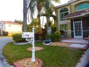 Front exterior featuring arched windows, screened entry, tile roof, and landscaped garden beds with decorative rock