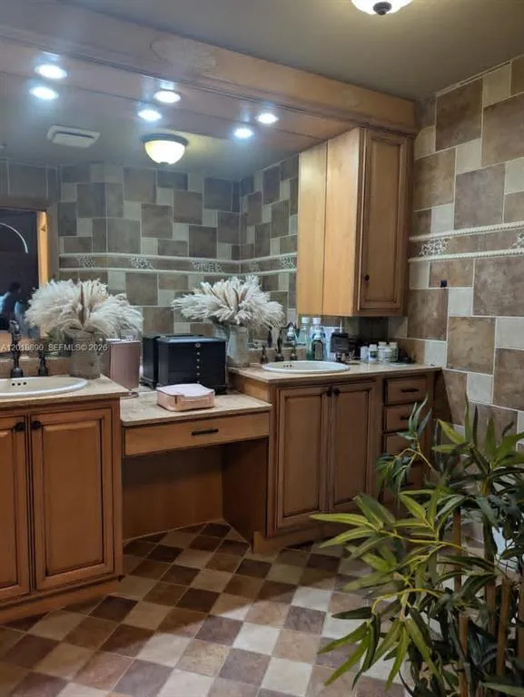 Dual vanity with undermount sinks, wood-finish cabinetry, built-in makeup desk, recessed lighting, and checkered tile flooring