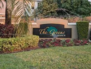 Community entrance signage with manicured landscaping, mature trees, and decorative shrubbery