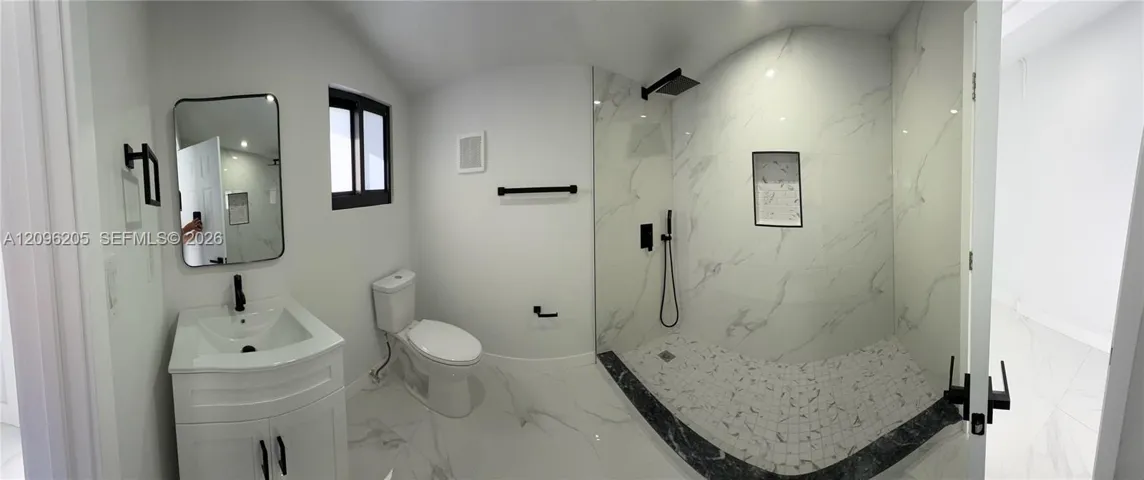 Bathroom featuring stone-finish flooring, a vanity with a rectangular sink, matte black hardware, and a walk-in shower with floor-to-ceiling tile surrounds and a built-in recessed niche