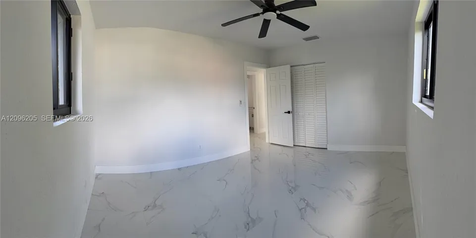 Interior room featuring large-format tile flooring with a neutral veined pattern, dual windows with dark frames, a ceiling fan, and a built-in closet with louvered doors