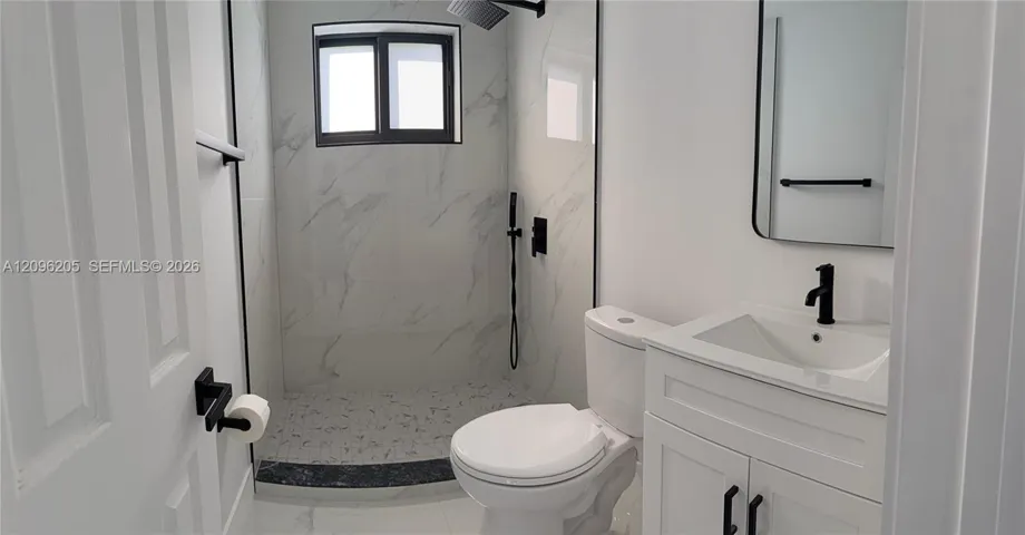 Bathroom featuring a walk-in shower with stone-patterned wall tile, a white vanity with a single basin, a matte black faucet, and a wall-mounted rectangular mirror