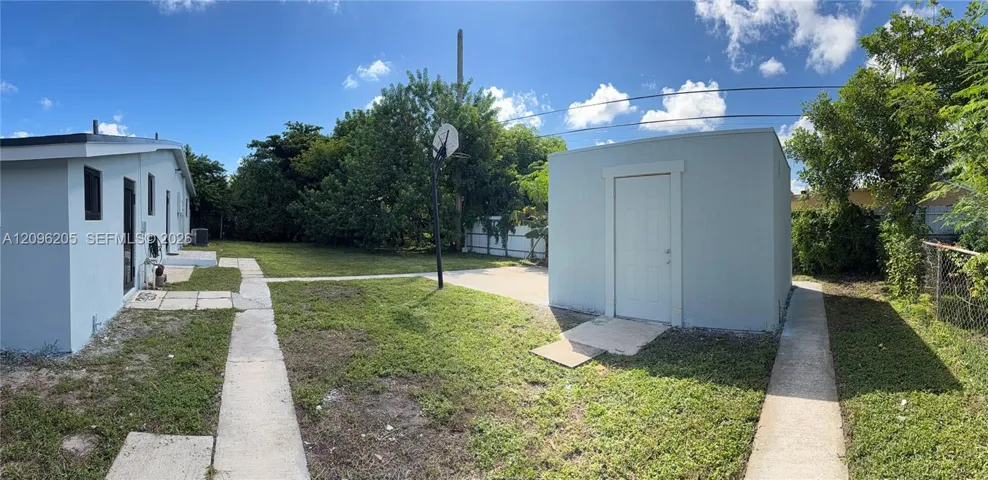 Rear yard featuring an expansive grass lawn, detached storage structure, concrete hardscaping, and mature perimeter trees