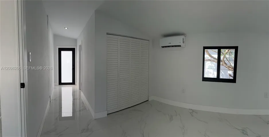 Interior space featuring large-format tile flooring with marble-pattern veining, bifold closet doors, a wall-mounted ductless air conditioning unit, and a black-framed glass-panel door