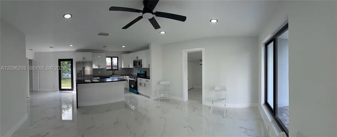 Open-concept kitchen featuring high-gloss cabinetry, stone-finish countertops, large-format tile flooring, recessed lighting, and a black ceiling fan