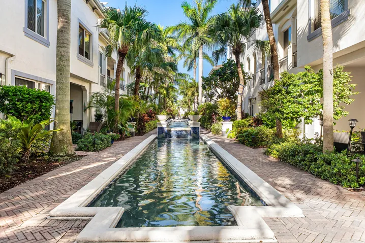 Elongated water feature with tiered fountain, surrounded by mature palm trees and lush landscaping
