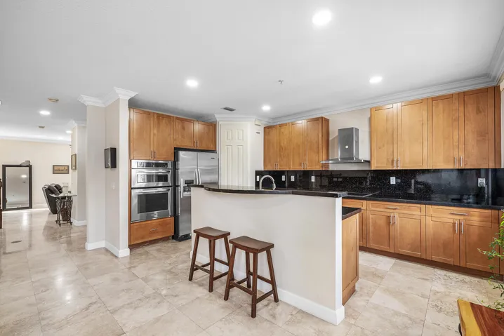Kitchen featuring wood-finish cabinetry, stainless steel appliances, granite countertops / backsplash, wall ovens and pantry