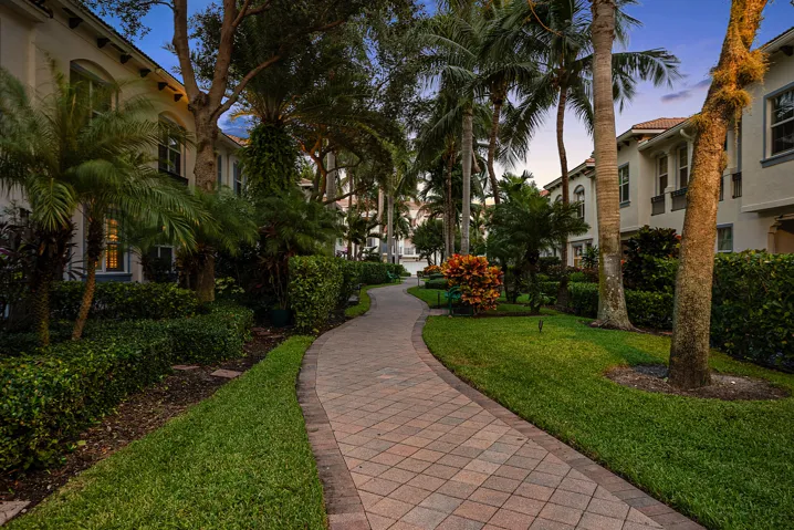 Paver pathway surrounded by manicured lawns, mature palm trees, and established hedges
