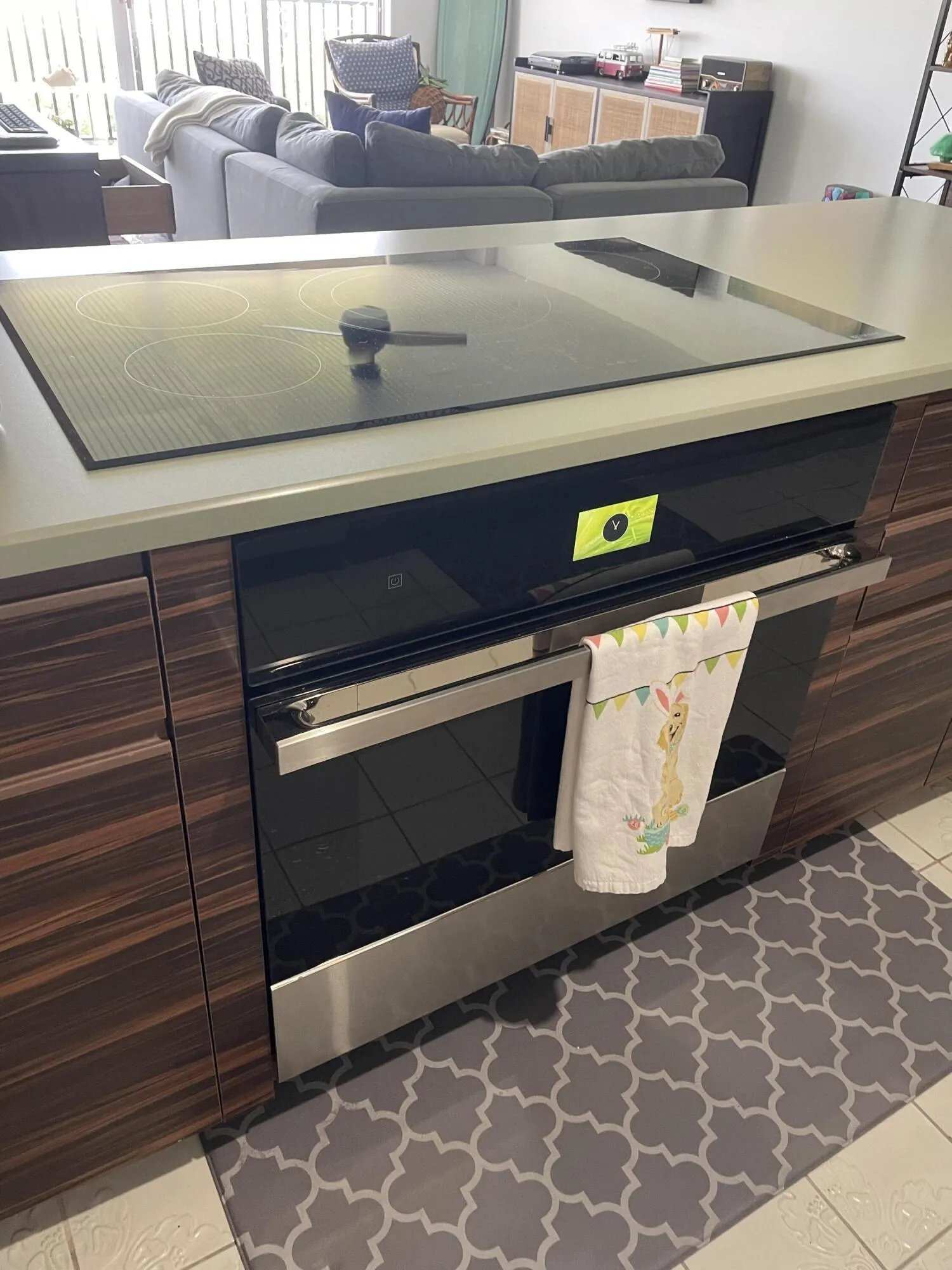 Built-in cooktop, integrated oven, wood-finish cabinetry, light-toned countertop, and tile flooring