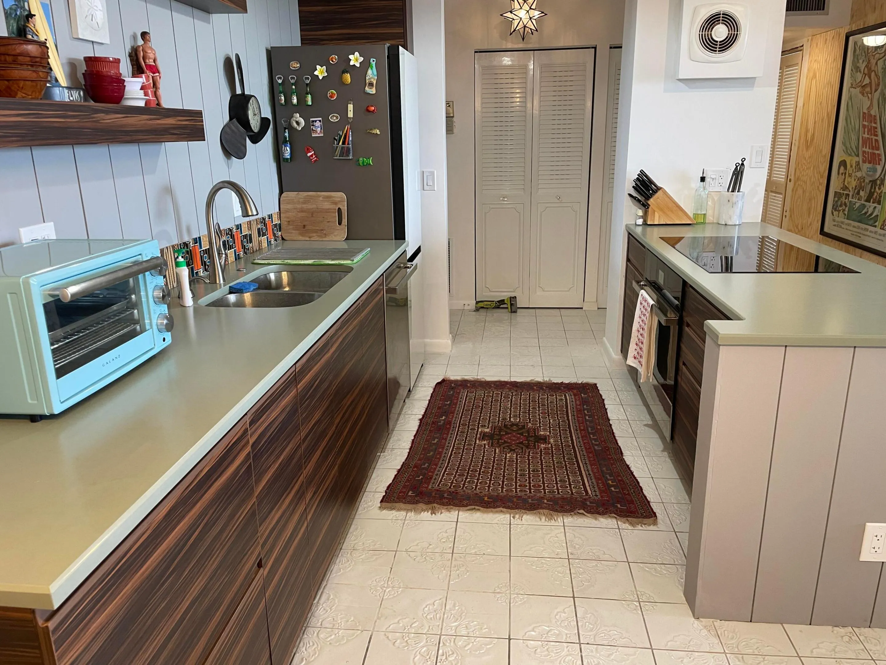 Galley kitchen featuring wood-finish cabinetry, light-toned countertops, a stainless steel sink with a gooseneck faucet, an integrated cooktop, and tile flooring