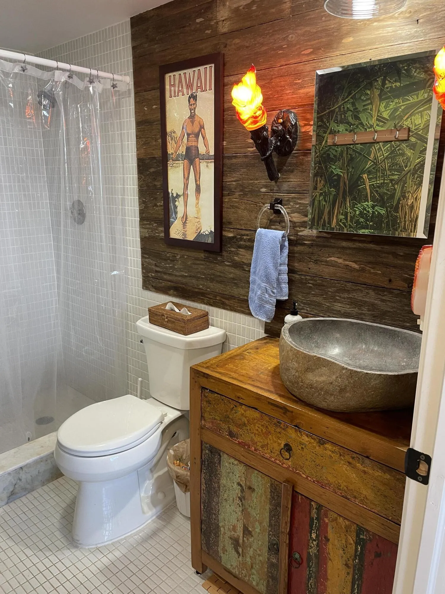 Wood-finish wall paneling, a vessel sink, a shower with a clear enclosure, white square floor tiles, and a rustic wood vanity with colorful paneling