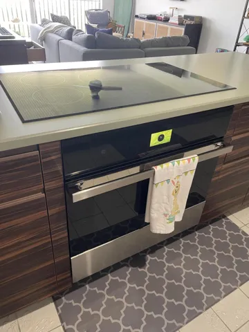 Built-in cooktop, integrated oven, wood-finish cabinetry, light-toned countertop, and tile flooring