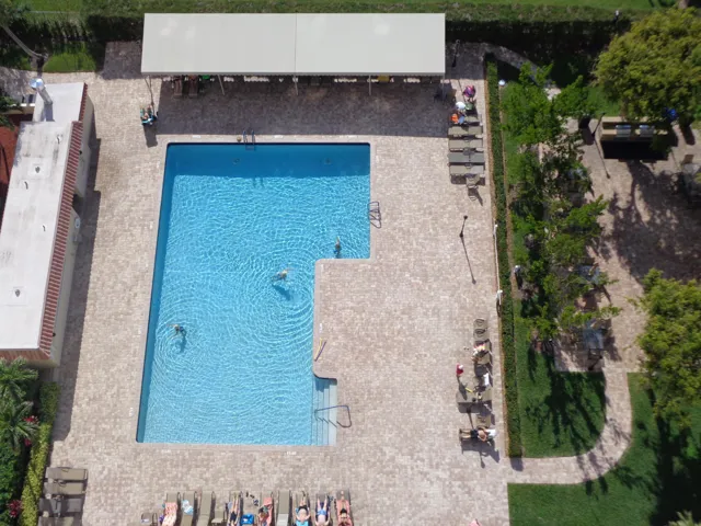 Rectangular swimming pool with integrated steps, surrounded by brick-finish paving, a covered lounge area, and manicured landscaping