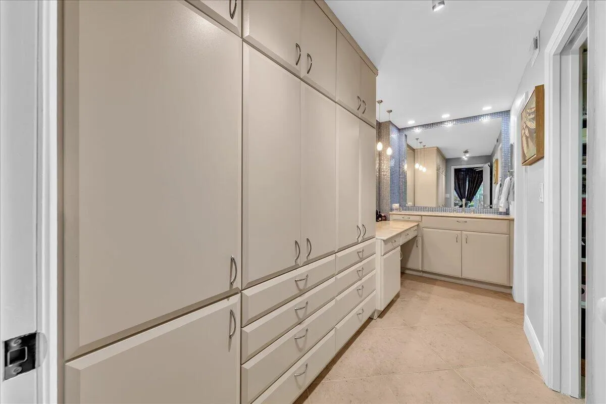 Extensive built-in cabinetry with ample storage, vanity with integrated countertop, large mirror, and recessed lighting
