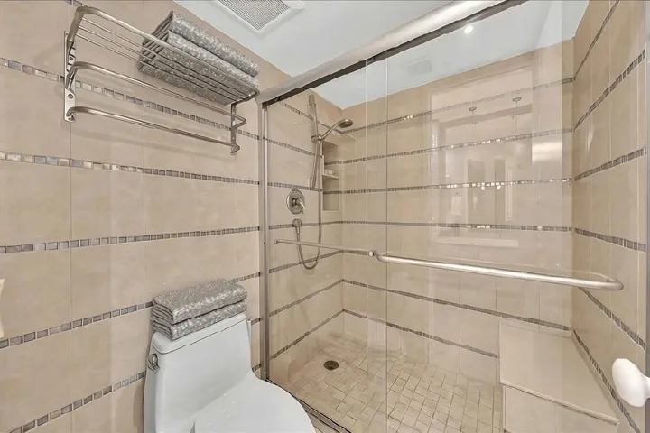 Glass-enclosed shower with a built-in bench and tiled walls with decorative mosaic accents