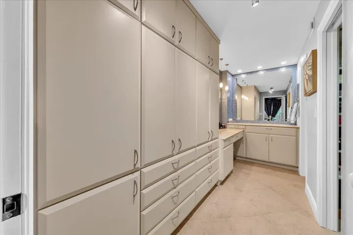 Extensive built-in cabinetry with ample storage, vanity with integrated countertop, large mirror, and recessed lighting