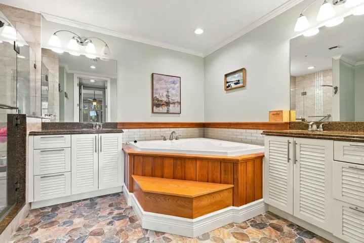 Primary bath has a spa-like feel with pebble-like flooring, built-in whirlpool tub, and custom shower