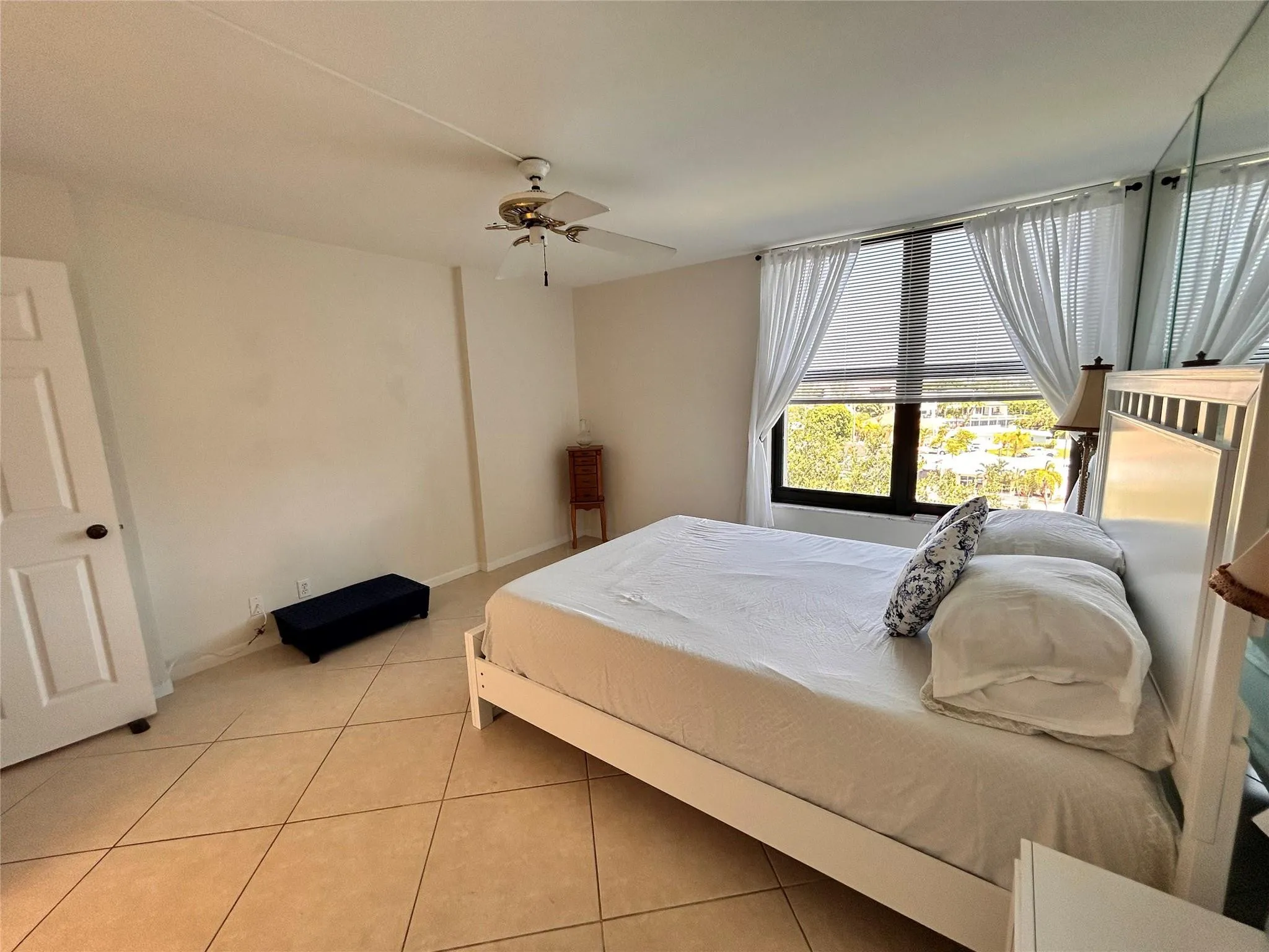 Travertine-style tile flooring, ceiling fan, and large window with blinds and sheer curtains