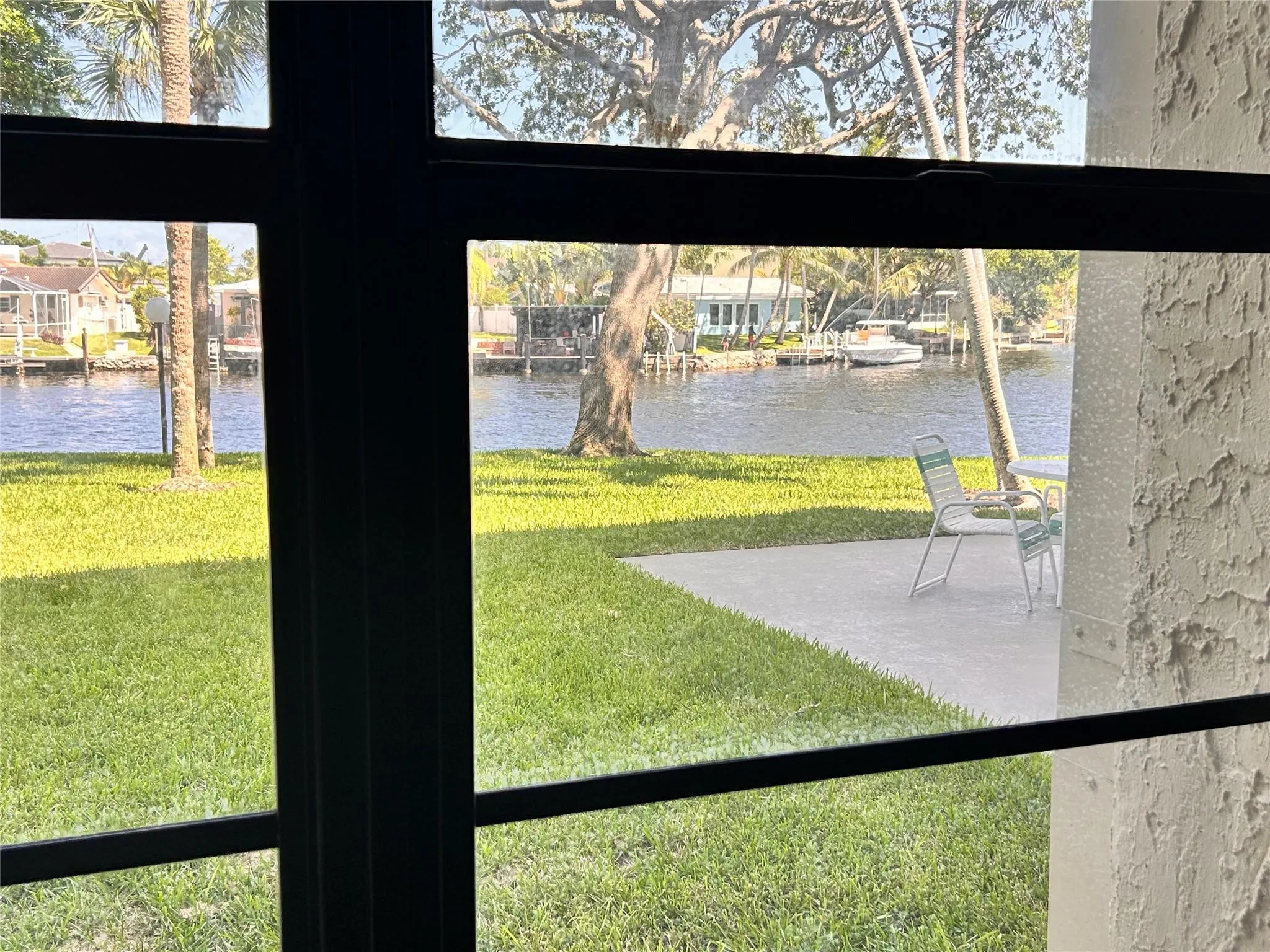 Waterfront property featuring a window with dark framing, a green lawn, and a concrete patio