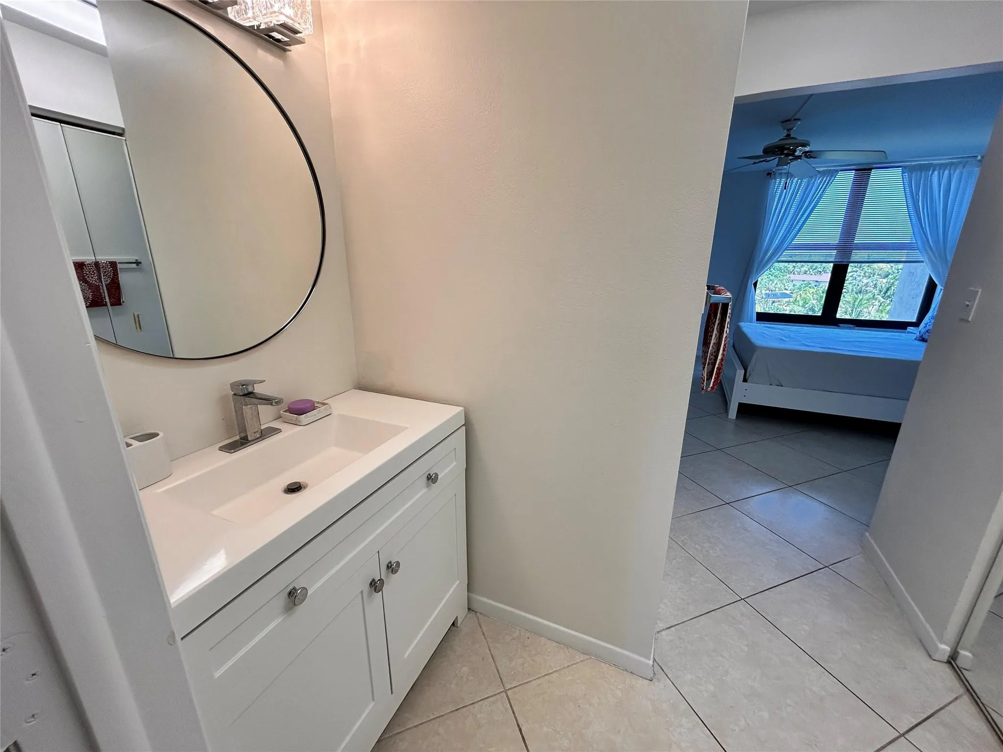 Bathroom featuring a white vanity with integrated sink, circular mirror, and modern light fixture