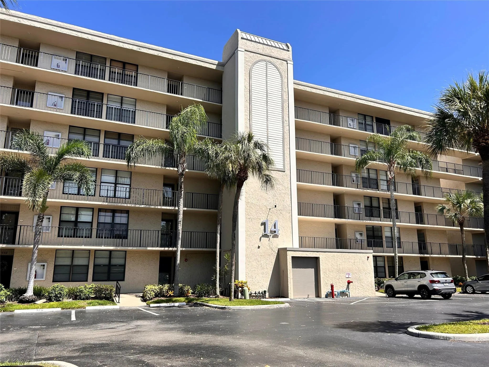 Multi-story building with a stucco exterior, multiple balconies featuring black railings, and a prominent central architectural column