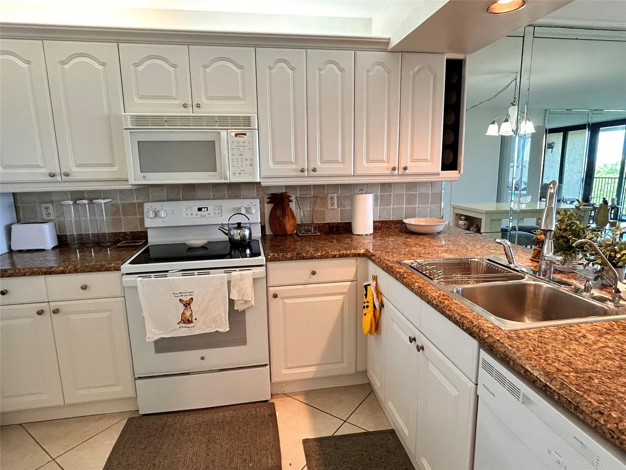 White cabinetry with decorative fronts, granite-style countertops, stainless steel double basin sink, and a built-in wine rack