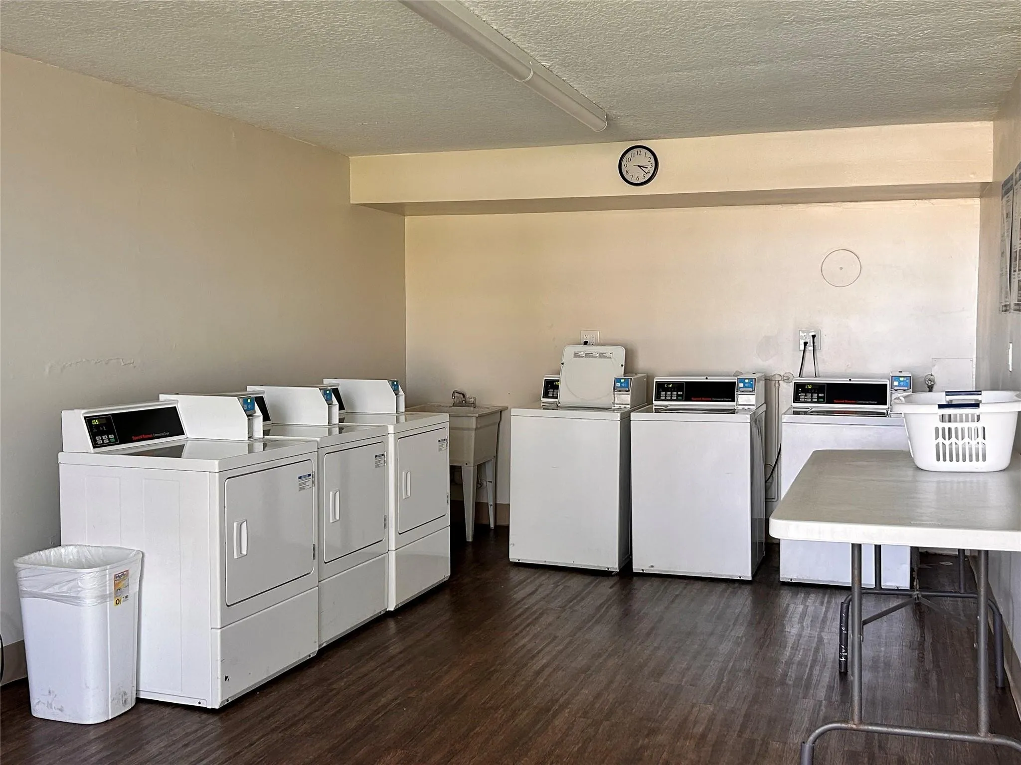 On-site laundry facility featuring multiple washers and dryers, utility sink, and wood-finish flooring