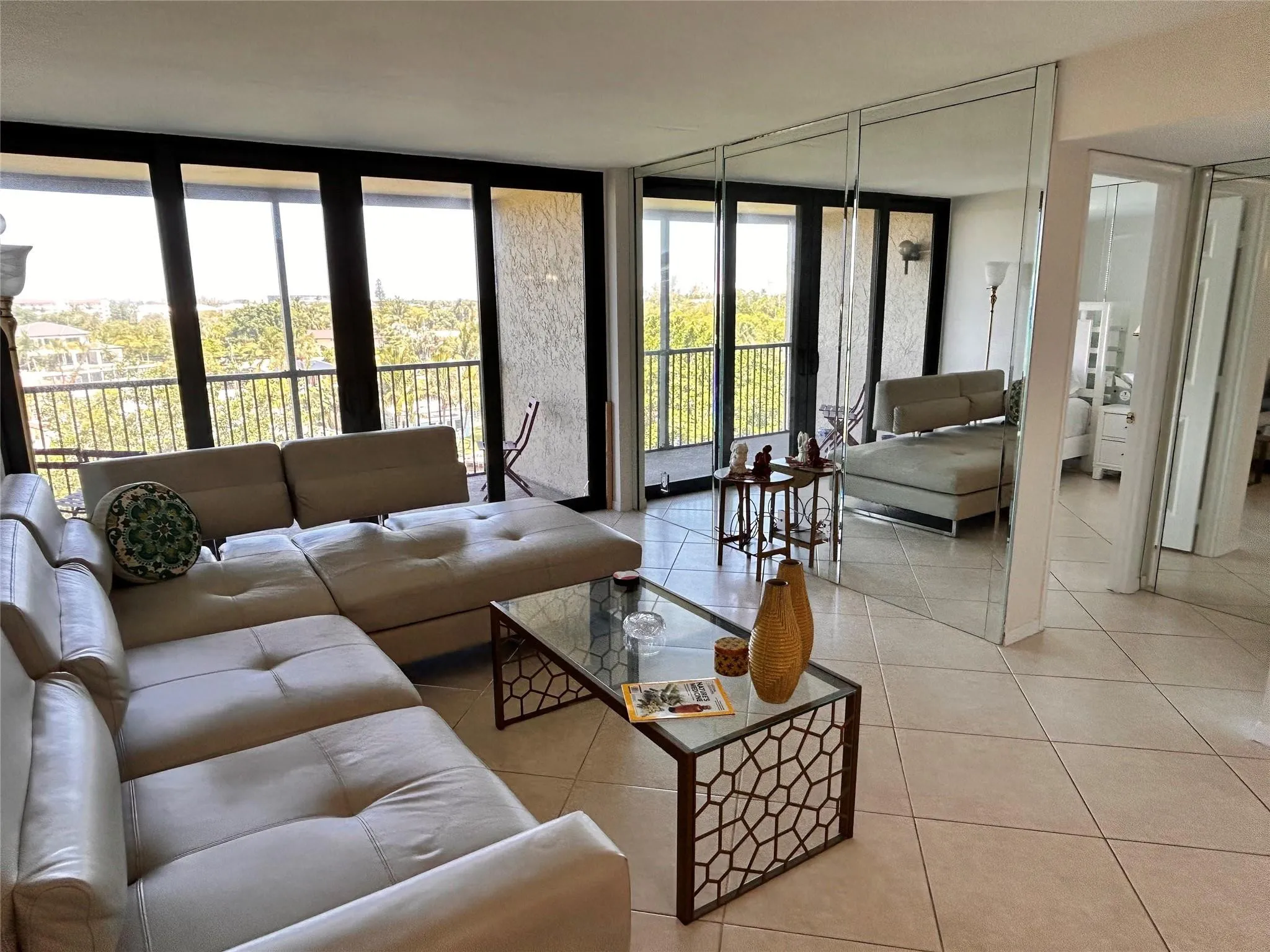 Expansive sliding glass doors, balcony with metal railing, floor-to-ceiling mirrored wall, and neutral-toned tile flooring