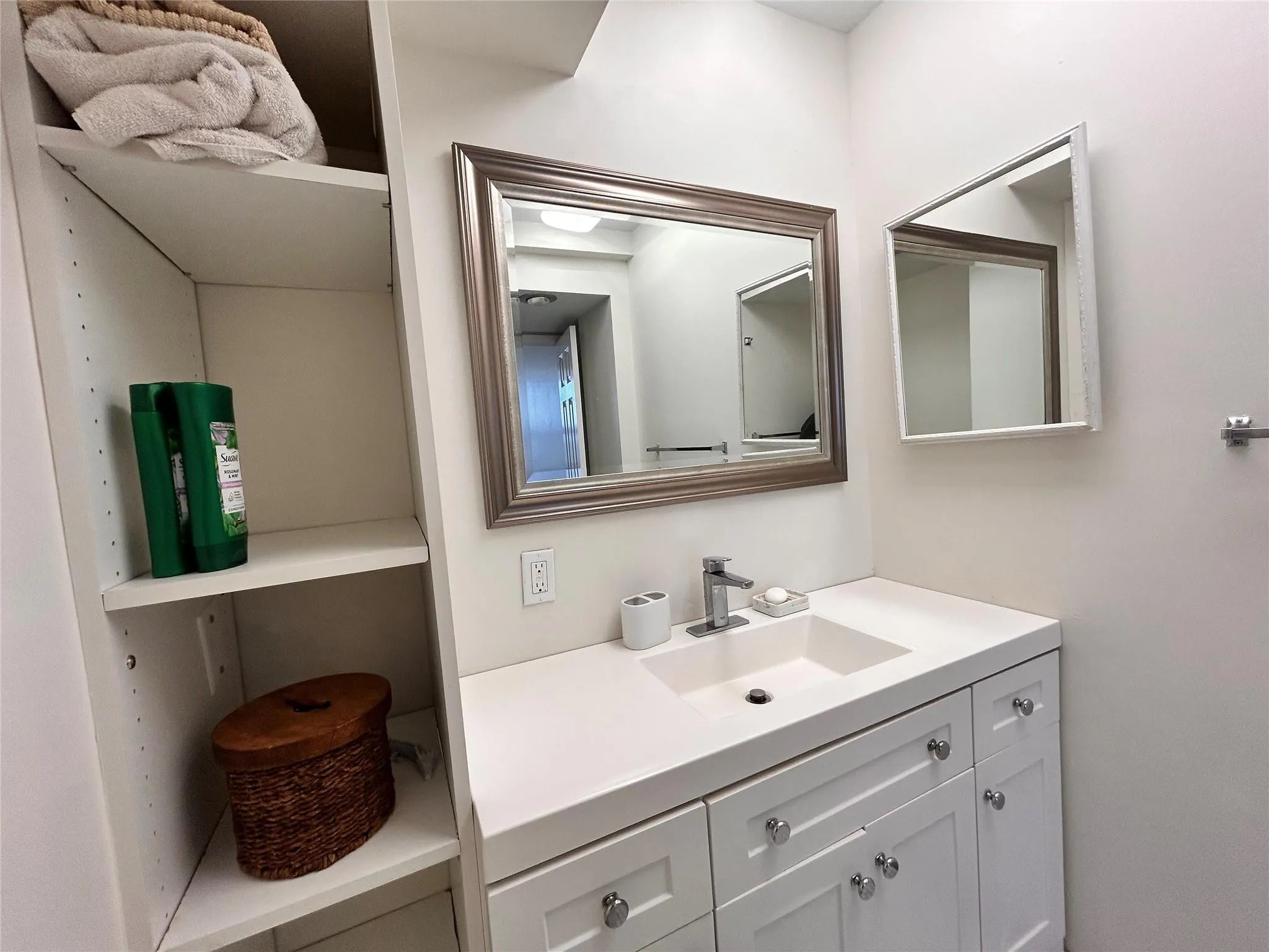 Built-in shelving, vanity with white shaker-style cabinetry, integrated sink, and an undermount faucet