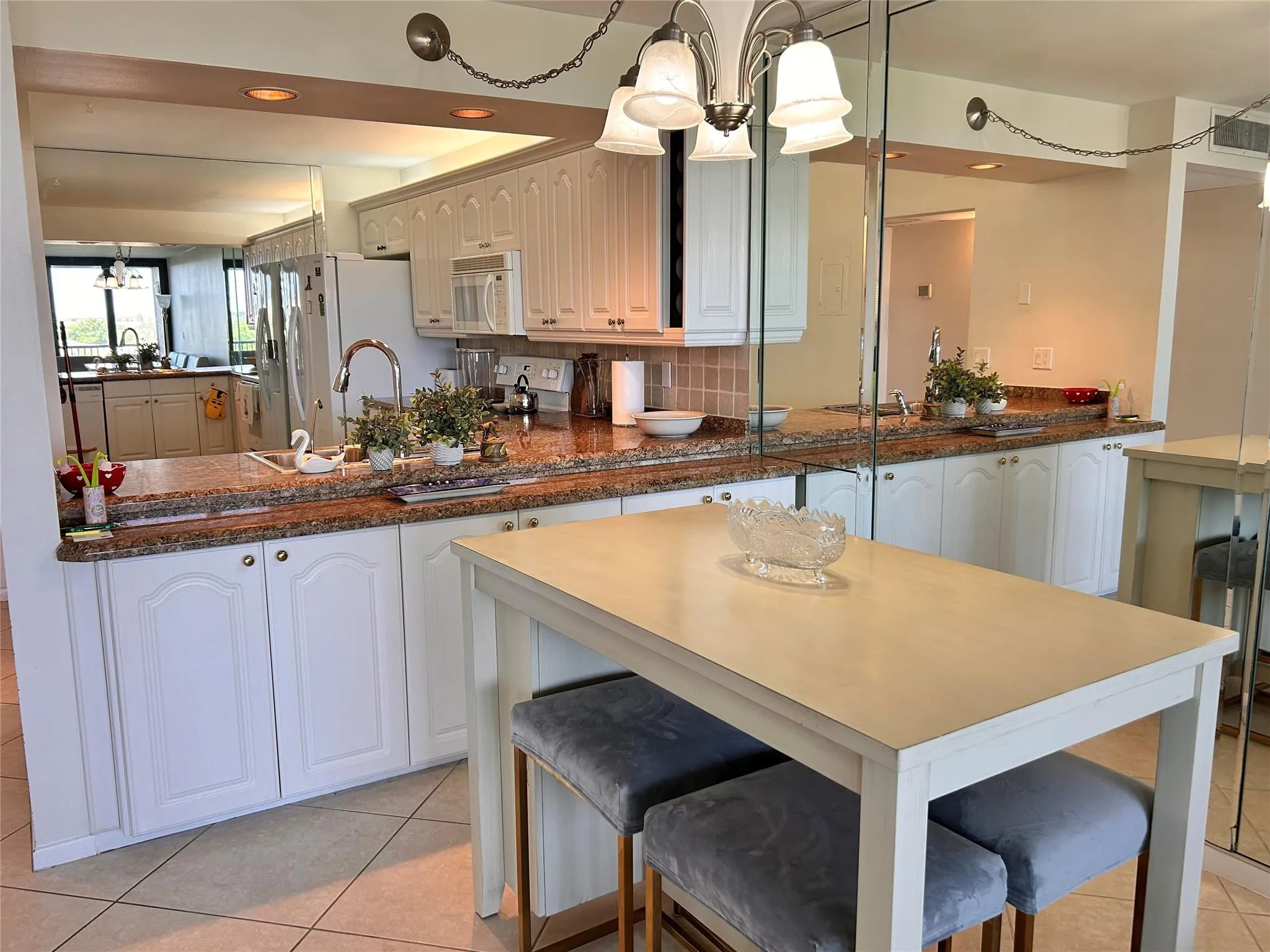Kitchen featuring white cabinetry, granite countertops, tile flooring, a stainless steel sink, and a multi-light chandelier