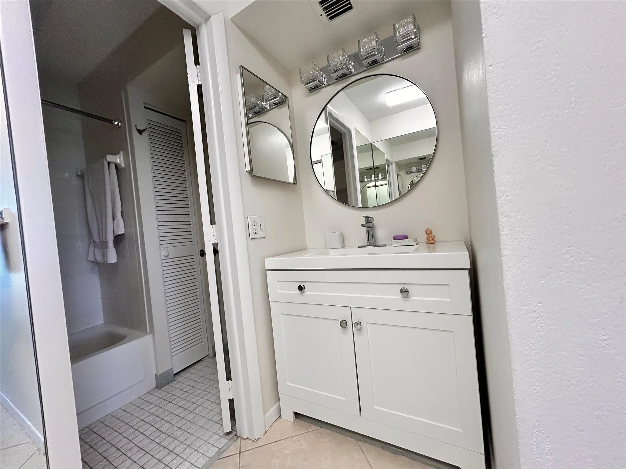 White vanity with chrome hardware, circular mirror, and multi-bulb vanity light