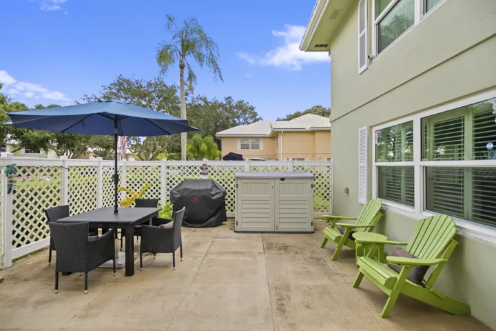 Private concrete patio with a white lattice fence, exterior stucco siding, and white-framed windows