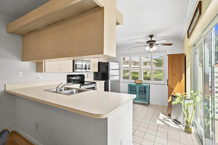 Kitchen featuring a built-in breakfast bar, light wood-finish cabinetry, stainless steel sink, and white tile flooring