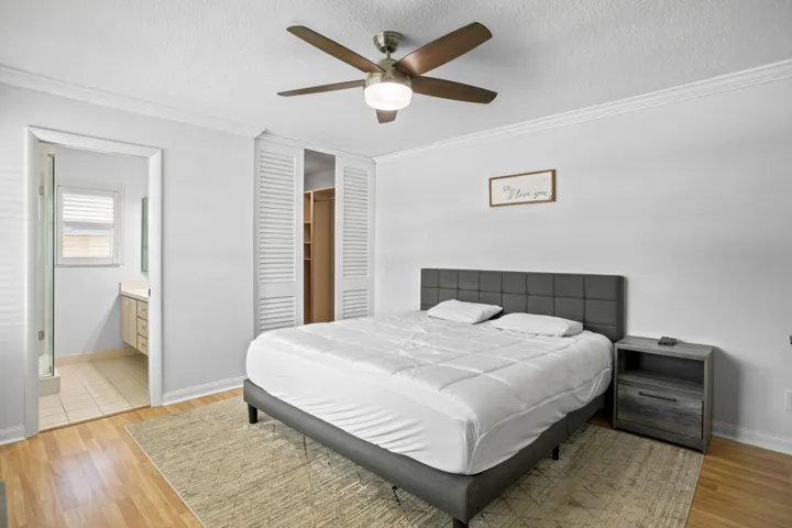 Wood-finish flooring, ceiling fan with integrated lighting, crown molding, and sliding louvered closet doors