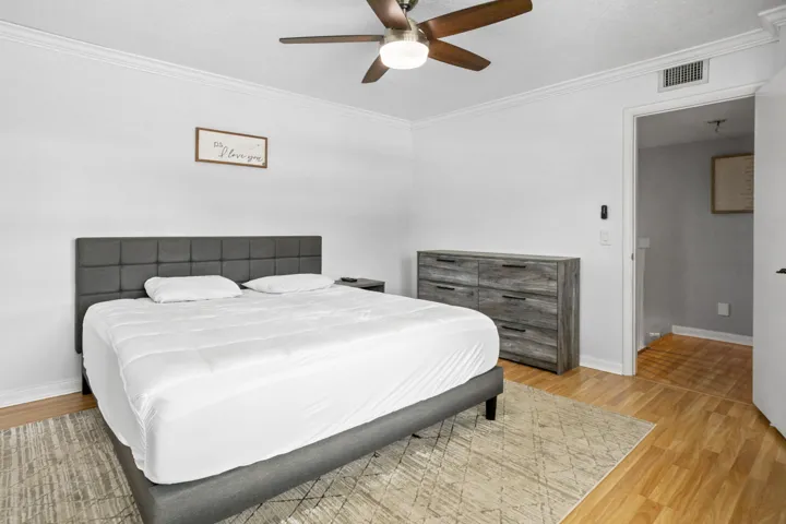 Wood-finish flooring with crown molding, white walls, and a ceiling fan with integrated lighting