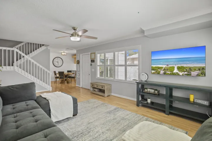 Open-concept living area featuring wood-finish flooring, a contemporary ceiling fan, and ample natural light from multiple windows