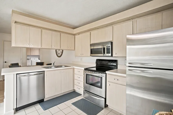 Kitchen featuring light wood-finish cabinetry, white countertops, stainless steel appliances, and white tile flooring